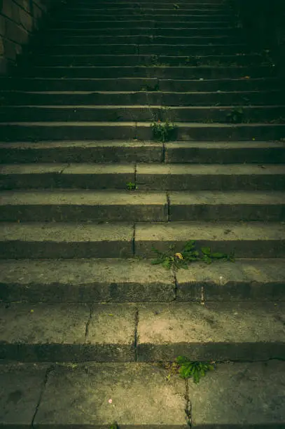 Photo of Wide staircase in a park made of natural stone with a handrail made of rusted steel in the dim light with a creepy and scary aura like in a thriller