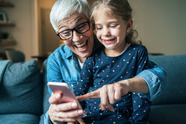 Portrait of grandmother and granddaughter Lovely little granddaughter having fun with modern grandmother using smartphone granddaughter photos stock pictures, royalty-free photos & images