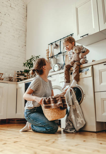 feliz familia madre ama de casa y el niño en la lavandería con lavadora - stereotypical housewife little girls family domestic kitchen fotografías e imágenes de stock