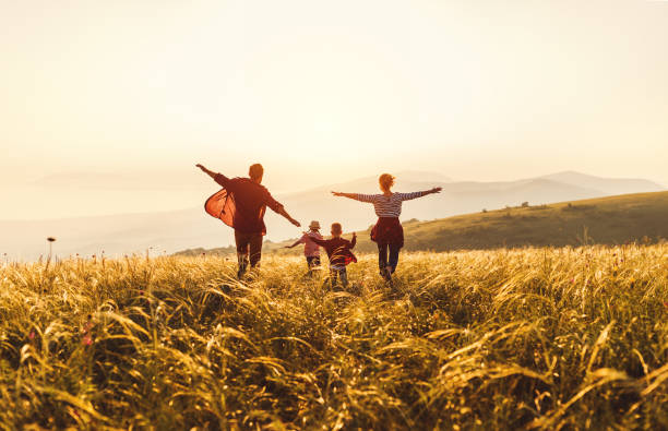 幸せな家族:母、父、子供の息子と娘が走り、日没に飛び乗る - 幸福 写真 ストックフォトと画像