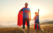 concept of father's day. dad and child daughter in hero superhero costume at sunset