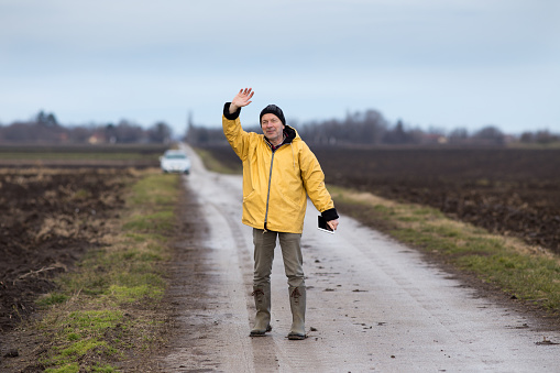 Mature farmer with tablet standing beside field and waving hand in winter time