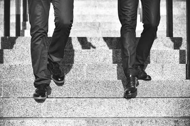 Photo of Close up legs of two businessman walking down stair in modern city