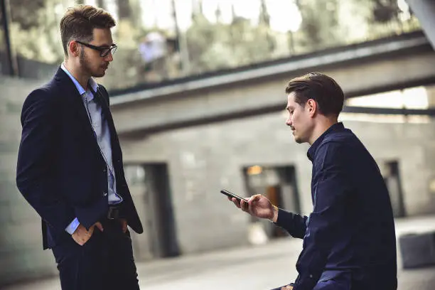 Photo of Bad news. Sad and frustrated young caucasian man sit at street and hold a phone.