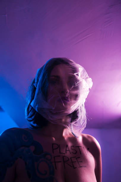 Plastic BAG on head: Suffocaterd Portrait of smiling female eco fighter wearing trash dress made of plastic and cardboard helping spread environment cleaning nature from pollution awareness concept - Vivid crazy neon saturated colors Violet Purple Blue - Other hands on her neck bolsa de plástico en la cabeza: retrato suffocaterd de mujer sonriente eco luchador usando vestido de basura hecho de plástico y cartón ayudando a difundir el medio ambiente limpiando la naturaleza de concepto de conciencia de la contaminación - vivo l