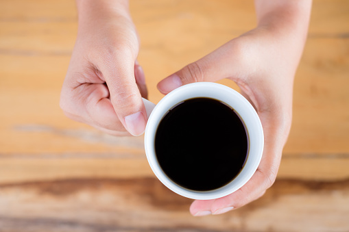 Closeup woman's hands hold the white cup of black coffee or americano coffee over the wood table, no sugar coffee for health