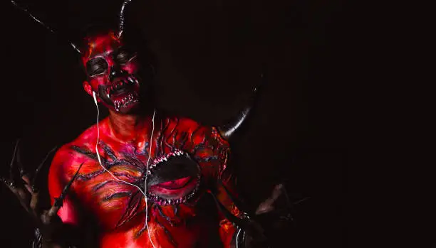 Photo of Evil or devil listening music by using earphones in darkness. Demon gets happy and closing eyes. Monster love listening nice song. It looks funny. Monster skin is red. Satan come from hell. copy space