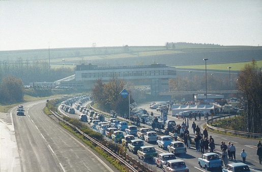 Thuringia, Bavaria, Franconian Forest East, Germany, 1989. Fall of the Berlin Wall. East German car column in November 1989 towards West Germany. Furthermore: motorway service area, West German helpers, spectators and vehicles of East German manufacture.