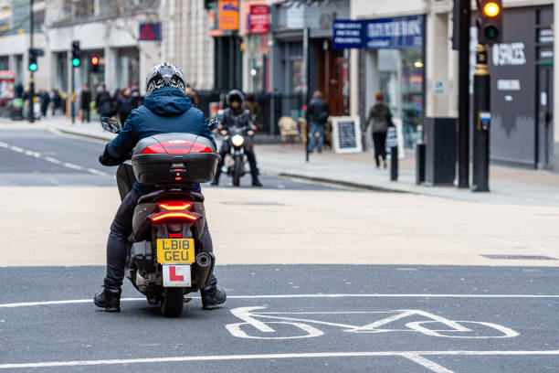 un homme sur un scooter attendant un feu de circulation à l’intersection du centre-ville, vue arrière, londres, angleterre, r-u - kensington gardens photos et images de collection