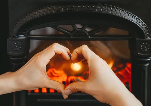 Hands shaped in a heart against a fireplace background. Closeup photo