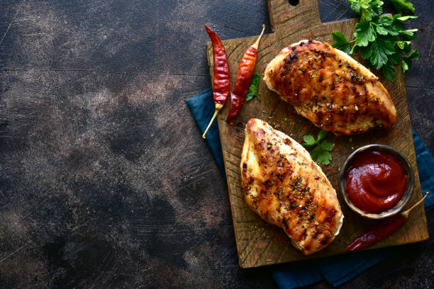 Grilled chicken fillet with spicy ketchup Grilled chicken fillet with spicy ketchup on a wooden cutting board on a dark slate, stone or concrete background. Top view with copy space. grilled chicken breast stock pictures, royalty-free photos & images