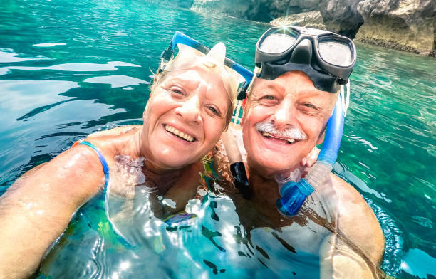 Happy retired couple with scuba mask taking selfie at tropical excursion - Boat trip snorkel experience in exotic scenarios - Elderly concept with active seniors traveling around world - Vivid filter feliz pareja jubilada con máscara de buceo tomando selfie en la excursión tropical - experiencia de snorkel viaje en barco en escenarios exóticos - concepto de ancianos con personas mayores activas que viajan alrededor del mundo - filtro vivo