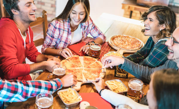 młodzi przyjaciele na prawdziwy śmiech podczas jedzenia pizzy w domu na spotkanie rodzinne - koncepcja przyjaźni z szczęśliwymi ludźmi korzystających razem bawiąc się razem w pizzeria picia piwowki - ciepły żywy filtr - pizza pizzeria friendship people zdjęcia i obrazy z banku zdjęć