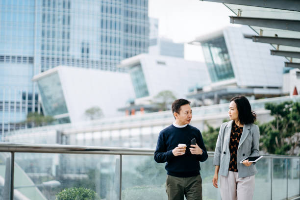 istock Two business persons using digital tablet and smartphone walking together and discussing on a business project outdoors against city scene in front of modern office buildings 1206651313
