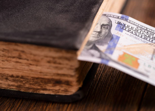 istock Hundred dollar bill inserted in an old book. Hundred dollar bill and book on a wooden table. 1206660366