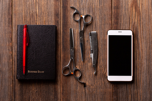 Hairdressing scissors and smartphone with a business diary on a wooden background.