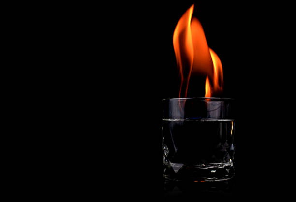istock Glass with vodka and fire flame on black background 1206661758