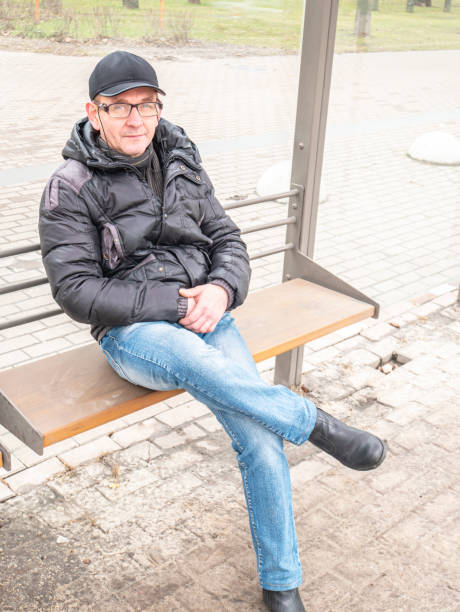 istock A man with glasses sits at a public transport stop. 1206661809