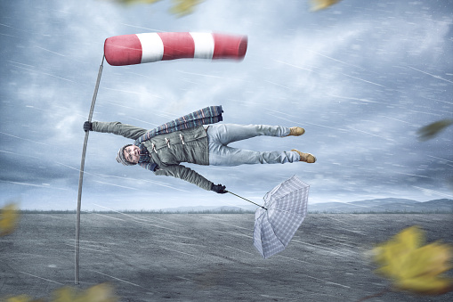 Funny compositing of a man holding on to a pole while being blown away by a storm. A windsock is attached to the pole.
