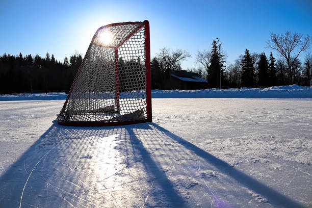 Sun silhouetting a empty hockey net on a frozen pond.
