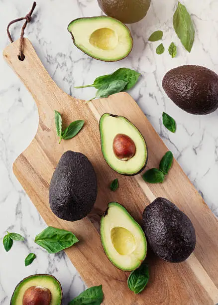 Whole avocados cut on a wooden board on top of a marble table