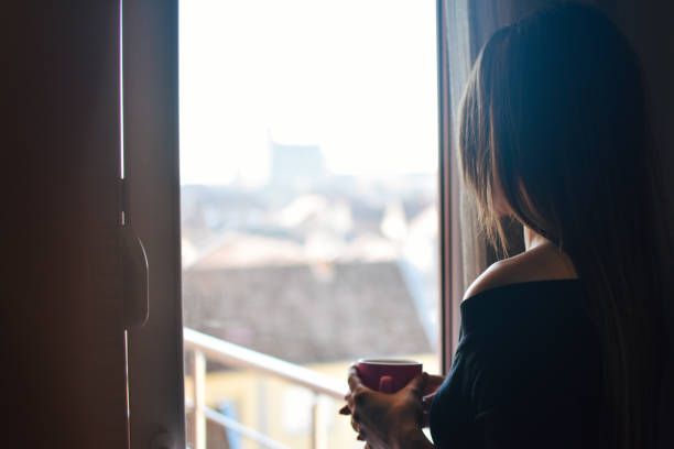 istock Woman standing by the window, with coffee cup in hands. 1206679439