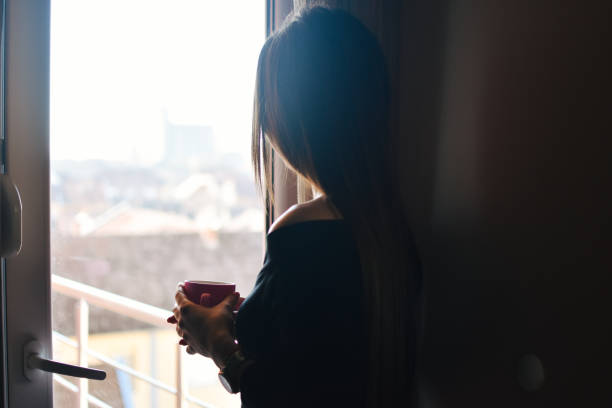 istock Woman standing by the window, with coffee cup in hands. 1206679590