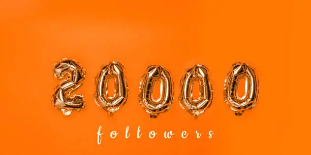 Photo of Air gold balloons in the form of numbers 20000 on orange background.