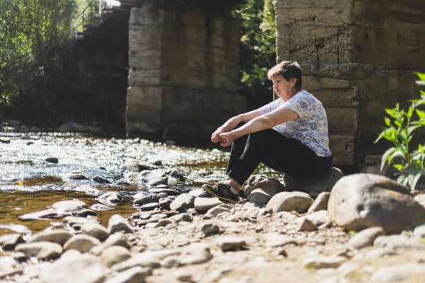 Senior woman sitting alone by a river on a bright day