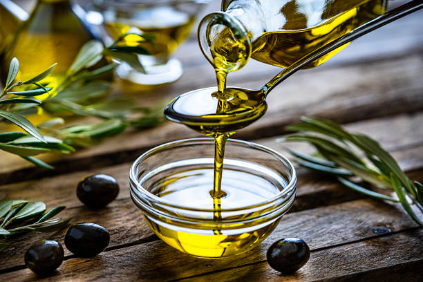 gießen von nativem olivenöl extra in einer glasschüssel - speiseöl stock-fotos und bilder