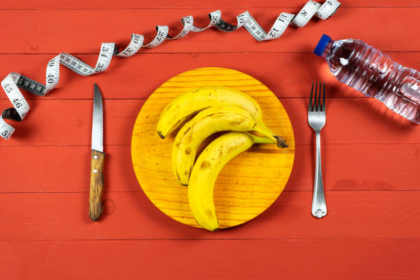 Ripe bananas on a wooden plate with cutlery on a red wooden table