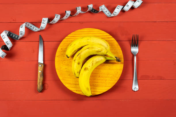 Ripe bananas on a wooden plate with cutlery on a red wooden table