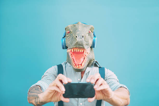 homme de mode aîné prenant le selfie avec le smartphone mobile tout en portant le masque de t-rex - type de hipster ayant la mascarade d’écoute de musique avec des écouteurs - concepts surréalistes drôles et absurdes - animal cell photos photos et images de collection