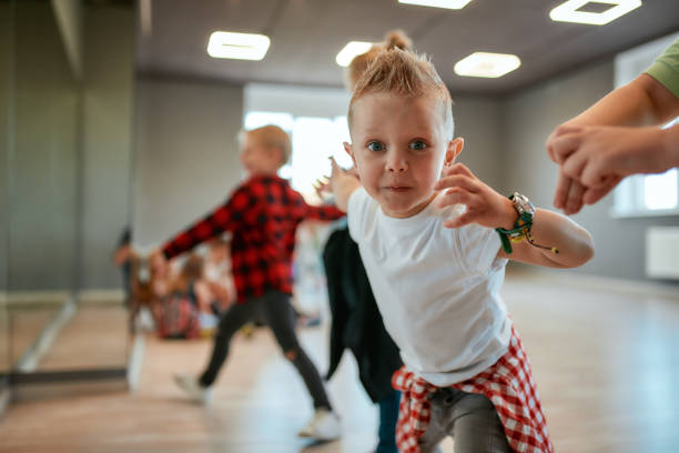 pieno di energia. bambino carino in t-shirt bianca che guarda la macchina fotografica e gesticola mentre ha un corso di coreografia nello studio di danza - top of the class foto e immagini stock