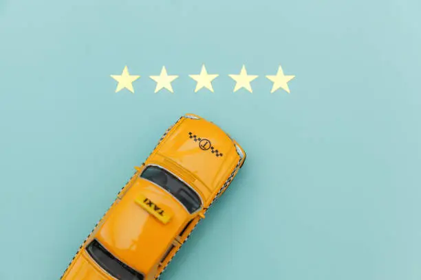 Photo of Yellow toy car Taxi Cab and 5 stars rating isolated on blue background. Smartphone application of taxi service for online searching calling and booking cab concept. Taxi symbol. Copy space