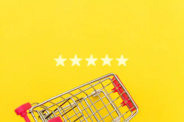 Photo of Small supermarket grocery push cart for shopping toy with wheels and 5 stars rating isolated on yellow background. Retail consumer buying online assessment and review concept