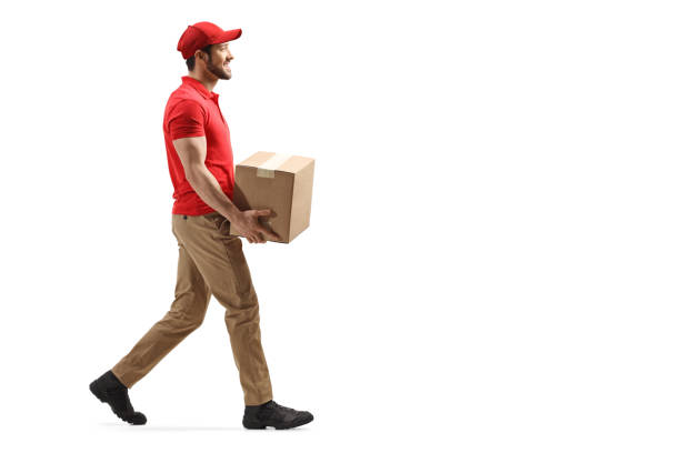 Delivery man carrying a package and walking Full length profile shot of a delivery man carrying a package and walking isolated on white background delivery person stock pictures, royalty-free photos & images