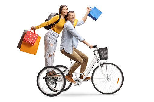 Young male and female on a tricycle with shopping bags isolated on white background