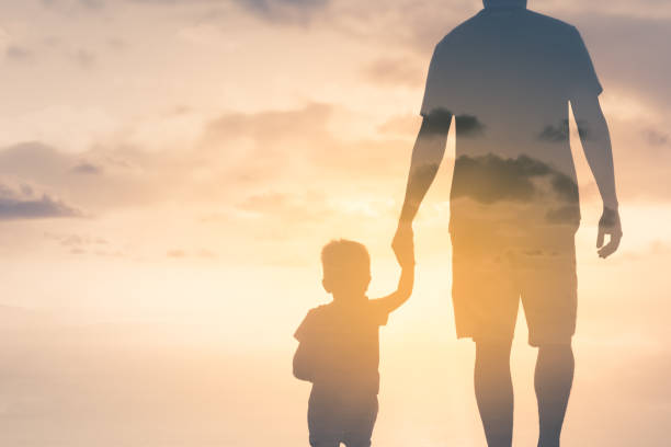 padre e hijo cogidos de la mano caminando hacia la puesta de sol dorada. - holding hands child silhouette family fotografías e imágenes de stock