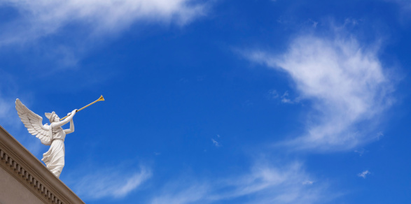 Angel with horn on blue sky background with white clouds