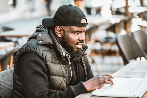 istock Happy black guy sitting at outdoor cafe with laptop computer 1206721644
