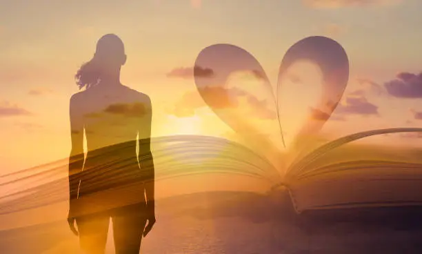 Photo of Heart shaped paper book against a beautiful sunset and silhouette of woman.