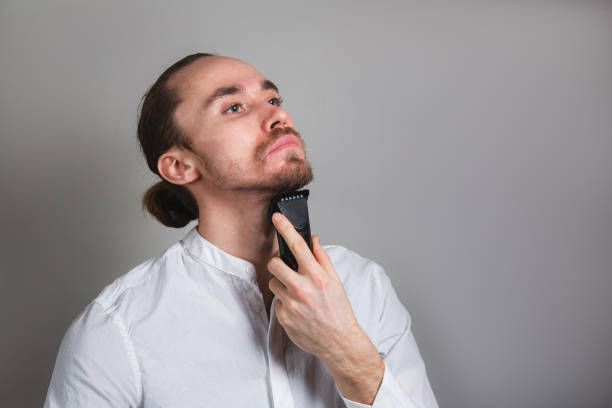 istock Man shaving face with electric razor on gray 1206723753
