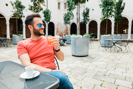 Young handsome man sitting in an outdoor cafe in summer time drinking coffee and cocktail