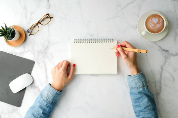 istock Woman write on the notebook for planner hand with coffee cup, smartphone, computer and stationary with copy space on marble table background. Top view. modern style. 1206729885