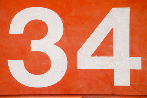 number 34 painted in white on an orange steel plate background, part of a tsunami barrier door in osaka japan