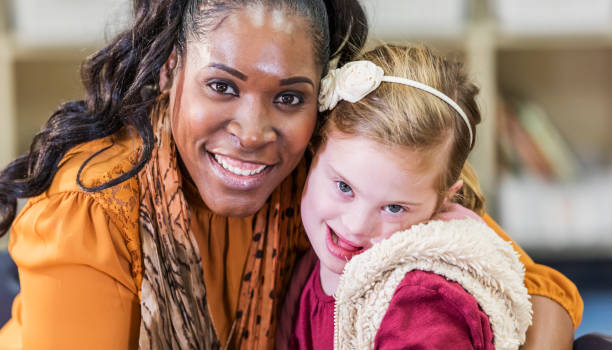 Girl with down syndrome, teacher in school A 9 year old girl with down syndrome with her elementary school teacher, smiling at the camera. The teacher is a mature African-American woman in her 40s. cheek to cheek photos stock pictures, royalty-free photos & images