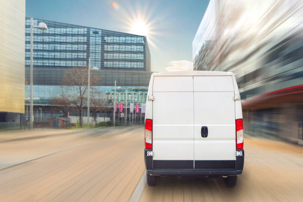 fourgonnette de livraison modifiée méconnaissable dans le centre-ville européen. le véhicule de messagerie moyen de minivan de camion livre le paquet à l’immeuble résidentiel de bureau dans le centre-ville. logistique d’expédition commerciale - van white delivery van truck photos et images de collection