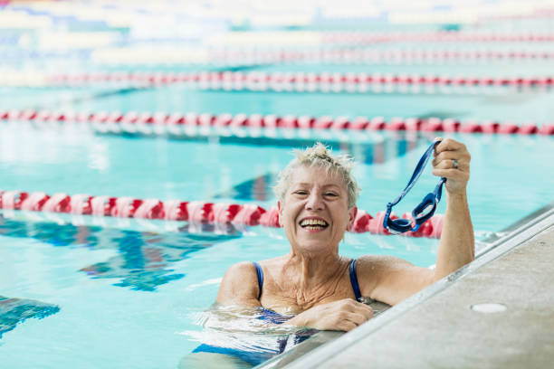 seniorin im pool macht pause von schwimmrunden - active seniors retirement enjoyment swimming pool stock-fotos und bilder
