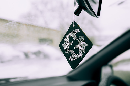 freshener in the car in the form of a drawing of the zodiac sign of a fish on a black square on the background of a snow-covered windshield.
